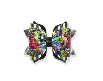 May include: A decorative hair bow featuring a colorful graphic print with characters. The bow has a black and white striped center and glittery black and silver accents. The bow is a fun accessory.