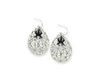 May include: A pair of Halloween-themed earrings. Each earring is teardrop-shaped with a cream-colored background and a black spiderweb design. A black spider is centered at the top of each earring, and the earrings have silver-colored hooks.