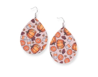 May include: A pair of teardrop-shaped earrings with a fall-themed pattern. The earrings feature a light pink background with orange pumpkins, donuts, coffee cups, and candy corn. The earrings have silver-colored hooks.