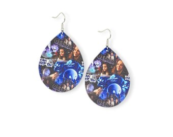 May include: A pair of teardrop-shaped earrings featuring a collage of images and text from the movie "Casper." The earrings have a silver hook and a blue and purple color scheme. The text "Can I Keep You?" is visible.