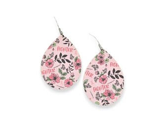 May include: A pair of teardrop-shaped earrings featuring a light pink background with a black floral pattern and the word FIGHTER printed in pink. The earrings include silver-toned metal hooks for attachment, showcasing a consistent design.