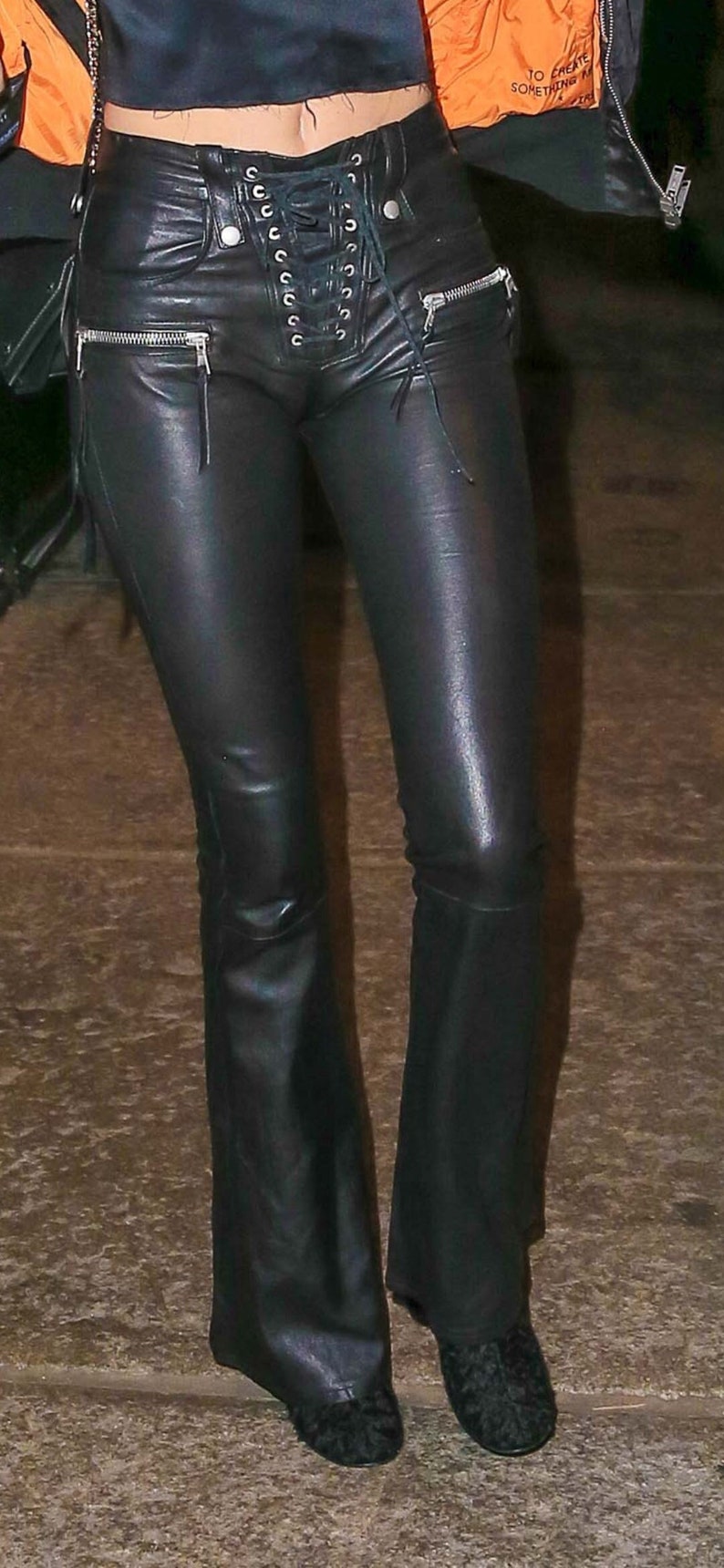 May include: Black leather pants with a lace-up detail at the front and a zipper detail on the sides. The pants are flared at the bottom.