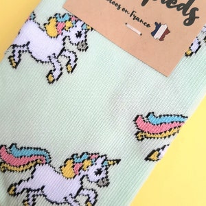 Può includere: Un paio di calzini verde chiaro con un motivo di unicorno bianco. I calzini hanno una criniera e una coda arcobaleno. I calzini sono realizzati in Francia.