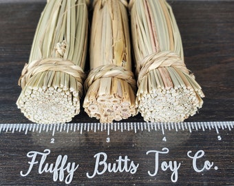 May include: Three natural brown and tan woven straw bundles, each tied with a brown twine, are lined up on a wooden surface. The bundles are approximately 4 inches in length.