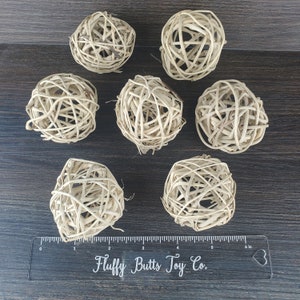 May include: Seven natural woven wicker balls, approximately 2 inches in diameter, on a brown wooden surface with a ruler that reads "Fluffy Butts Toy Co."
