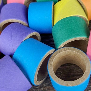 May include: A collection of colorful cardboard tubes, each painted in a different solid color, including purple, blue, green, yellow, and pink. The tubes are stacked and arranged in a random pattern.