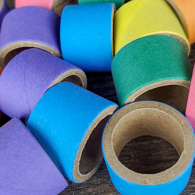 May include: A collection of colorful cardboard tubes, each painted in a different solid color, including purple, blue, green, yellow, and pink. The tubes are stacked and arranged in a random pattern.