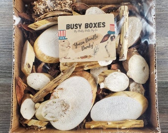 May include: A cardboard box filled with a variety of natural dog chew toys. The box is labeled "Busy Boxes by Fluffy Butts Joy Co." and "Yucca Doodle Dandy".