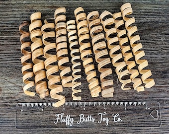 May include: A close-up of a group of 15 natural wood, brown, curled, and twisted pieces of wood. The wood pieces are arranged in a row and are approximately 6 inches long. A clear ruler with the text "Fluffy Butts Toy Co." is below the wood pieces.