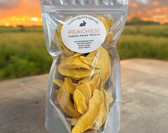 May include: A clear plastic bag filled with freeze-dried peach slices. The bag has a white label with the text "FLUFFY BUTTS TOY CO. PEACHES! FREEZE DRIED TREATS NO PRESERVATIVES. NO ADDITIVES. NO FILLERS. JUST FRUIT!"