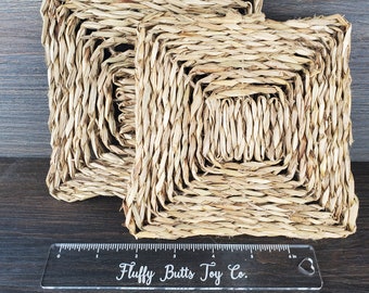 May include: Two square woven seagrass mats, one slightly larger than the other, with a ruler that reads "Fluffy Butts Toy Co." in black lettering. The mats are made of natural, light brown seagrass and are perfect for small animal enrichment.