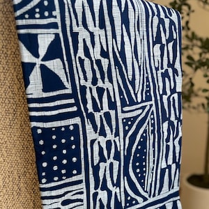 May include: A rectangular fabric textile featuring a deep navy blue background with a white geometric pattern consisting of stripes, dots, and abstract shapes. A small brown rectangular tag with the text WAX is attached to the bottom edge.