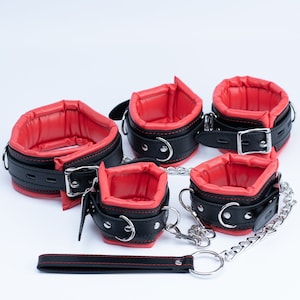 May include: Set of five black leather restraints with red padded lining. The restraints are connected by a silver chain and include a separate black leather strap.