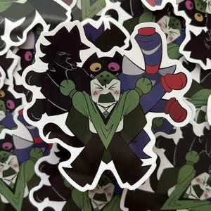 Puede incluir: Una colección de pegatinas con personajes de dibujos animados en varias poses. Las pegatinas muestran un personaje verde con una expresión severa, una silueta negra y un personaje azul con guantes rojos. Las pegatinas tienen un borde blanco.