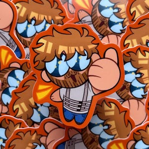 May include: A die-cut sticker featuring a cartoon character with brown hair, a beard, and large blue sunglasses. The character wears a white shirt with horizontal gray stripes and blue pants, giving a thumbs-up gesture against an orange background.