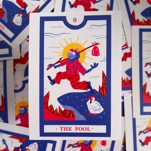 Może przedstawiać: Ilustracja karty tarota "Głupiec" z kapryśną postacią w czerwonym stroju w kratę, niosącą torbę na kiju. Karta ma niebieską obwódkę, żółte słońce i numer "0" na górze. Tekst "THE FOOL" znajduje się na dole.