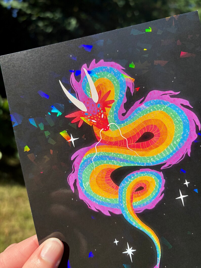 May include: A rainbow dragon with pink accents on a black background with iridescent glitter. The dragon is curled up with its head facing the viewer.