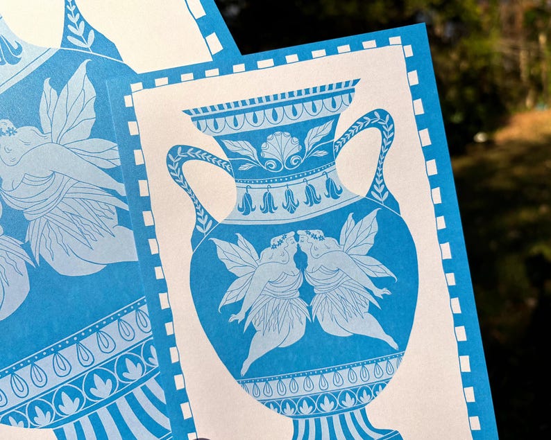 May include: Blue and white art print featuring a classical vase design. The vase is adorned with floral and shell motifs, and two figures with wings are kissing. The print has a border with a repeating pattern.