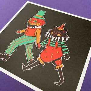 May include: A black cat and a pumpkin-headed figure wearing colourful costumes. The cat is wearing a red and green striped shirt with a red and white polka dot overall. The pumpkin-headed figure is wearing a green and red striped shirt and trousers. Both figures are smiling.