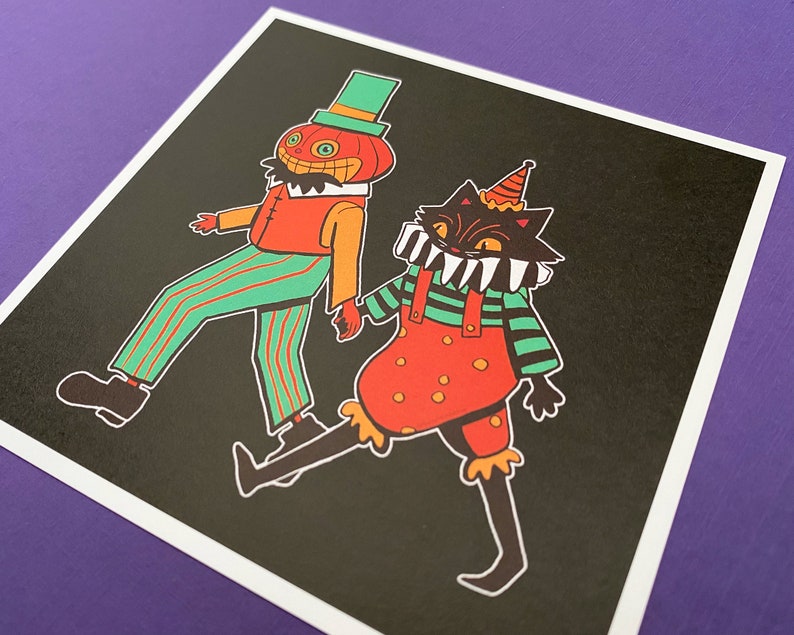 May include: A black cat and a pumpkin-headed figure wearing colourful costumes. The cat is wearing a red and green striped shirt with a red and white polka dot overall. The pumpkin-headed figure is wearing a green and red striped shirt and trousers. Both figures are smiling.