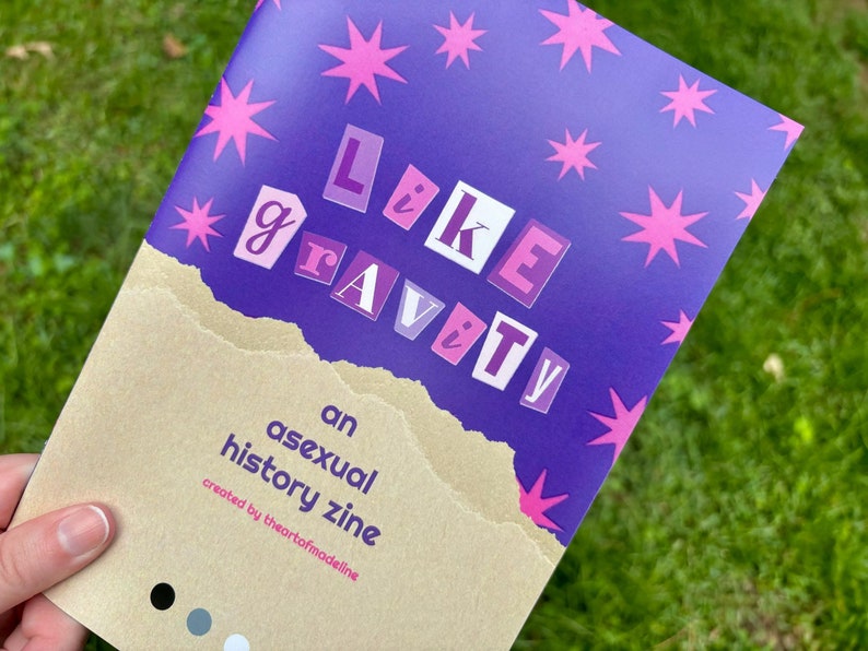 以下が含まれることがあります： ピンクの星と「Like Gravity」というタイトルが切り抜かれた文字で書かれた紫色の雑誌。下のテキストには「an asexual history zine created by theartofmodelling」と書いてあります。
