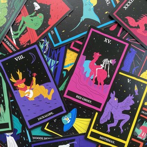May include: A set of playing cards with black backgrounds and colorful illustrations of mythical creatures. The cards feature names like "Bigfoot", "Jackalope", "Red Ghost", "Mothman", and "Death Worm".