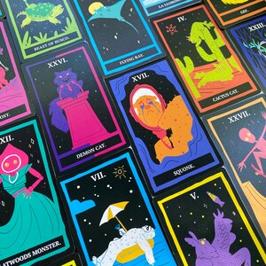 May include: A set of 10 tarot cards with black backgrounds and colorful illustrations. The cards feature various creatures and characters, including a beast, a flying ray, a demon cat, a cactus cat, a squonk, and a monster. The cards are numbered with Roman numerals.