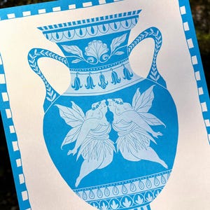 May include: A blue and white print featuring a classical vase design. The vase is adorned with floral and geometric patterns, and depicts two winged figures kissing. The print has a white border with blue square accents.