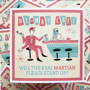 Op de afbeelding: Vierkante print met een retro café-illustratie. De woorden "HI-WAY CAFE" staan bovenaan, met een man in een roze pak en een ober. De tekst onderaan luidt "WILL THE REAL MARTIAN PLEASE STAND UP?"