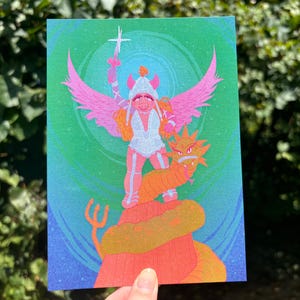 May include: A colorful art print featuring a whimsical illustration of a pig-like character with pink wings, a helmet, and a sword, standing atop a dragon. The artwork has a vibrant color palette with shades of pink, orange, green, and blue.