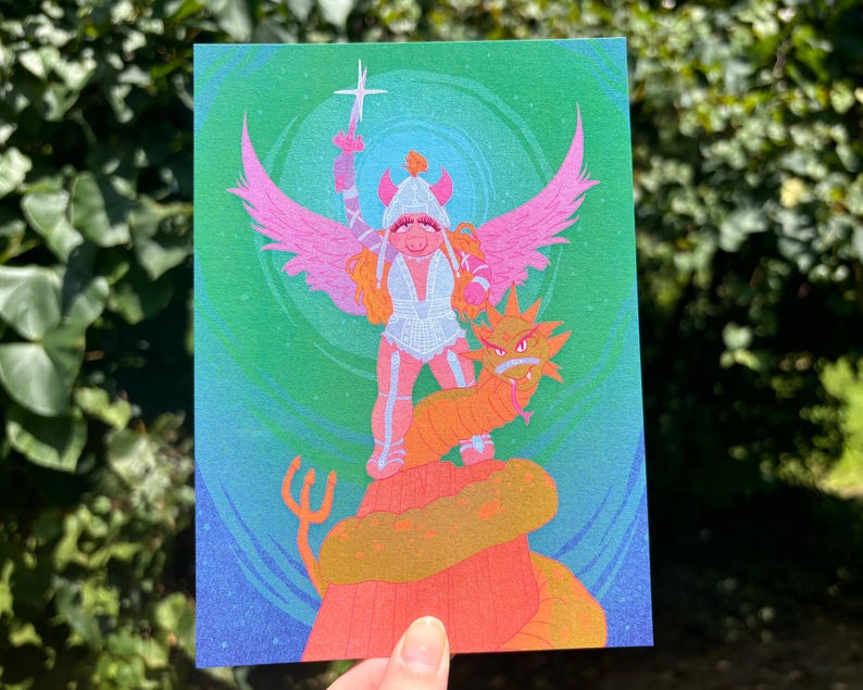 May include: A colorful art print featuring a whimsical illustration of a pig-like character with pink wings, a helmet, and a sword, standing atop a dragon. The artwork has a vibrant color palette with shades of pink, orange, green, and blue.