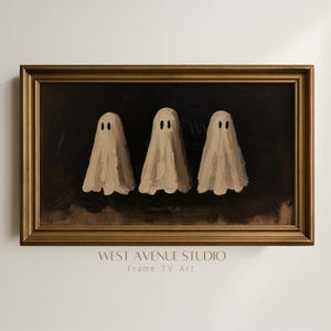 May include: A rectangular framed wall art piece featuring an oil painting of three beige ghosts with dark oval eyes against a dark brown background. The frame is a metallic gold with a classic moulded profile. Text below reads WEST AVENUE STUDIO.