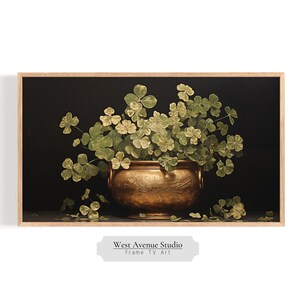 May include: A painting of a golden pot filled with green shamrocks against a dark background. The pot has intricate details and the shamrocks are arranged in a lush, natural way. The painting is framed in a light wood frame.