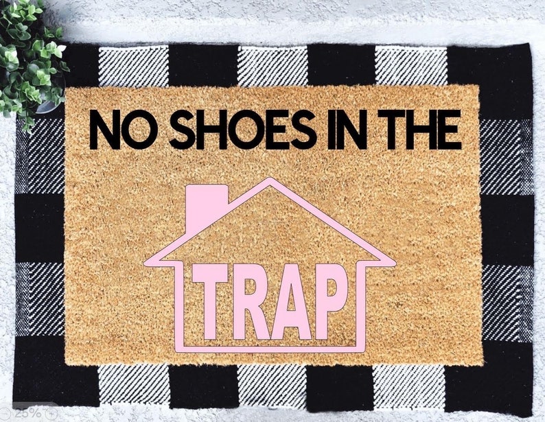 Peut inclure: Un paillasson brun avec une bordure &agrave; carreaux noirs et blancs. Le paillasson porte le texte "NO SHOES IN THE TRAP" en lettres noires et une maison rose avec le mot "TRAP" &agrave; l'int&eacute;rieur.