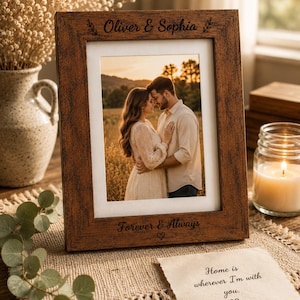 Puede incluir: Un marco de fotos rectangular de madera con un acabado texturizado marrón oscuro. La parte superior está grabada con "Oliver & Sophia" y la inferior con "Forever & Always" y un corazón. Contiene la foto de una pareja y un borde blanco.