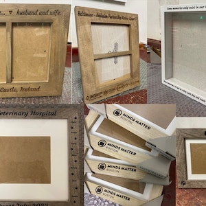 May include: Assortment of wooden picture frames with various engravings. Some frames are natural wood, others are painted white. The engravings include "Best friends for life... husband and wife", "Dunluce Castle, Ireland", "Barry Veterinary Hospital", "Baltimore-Fakkalon Partnership Kitchen Cohort", "Some memories only exist in our heart forever", "MINDS MATTER BOSTON", "OSCAR", and "FUZZ".
