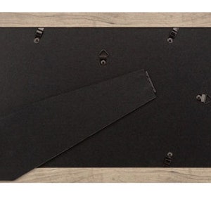 May include: A light brown wood picture frame with a black mat and a sawtooth hanger on the back.