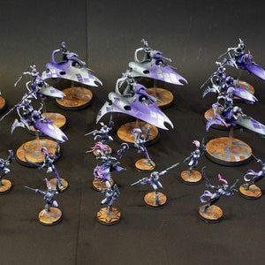 May include: A collection of purple and silver painted miniature figurines, including a group of winged warriors riding on flying mounts and a group of standing warriors. The miniatures are arranged on a black surface.