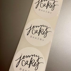 Może przedstawiać: Trzy białe okrągłe naklejki z czarnym tekstem, który brzmi "jenny cakes bakery" w pisanym odręcznie stylu.