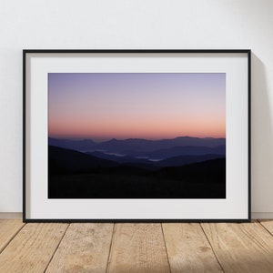 May include: A framed photograph of a mountain range at sunrise. The sky is a gradient of purple, pink, and orange. The mountains are silhouetted against the sky.