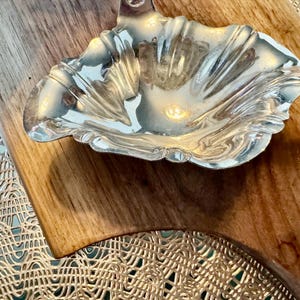 May include: A silver, ornate, decorative dish with a scalloped edge sits on a wooden surface.