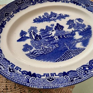 K&ouml;nnte beinhalten: Eine wei&szlig;e ovale Servierplatte mit einem blauen und wei&szlig;en Weidenmuster. Das Muster zeigt eine Pagode, B&auml;ume und eine Br&uuml;cke.