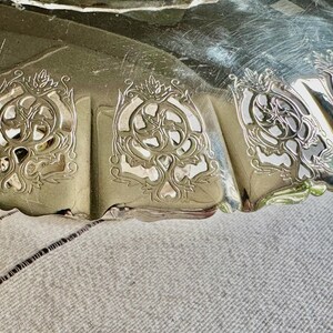 May include: Close-up of a silver-colored, ornate serving dish. The dish has a scalloped edge and decorative cut-out designs. The intricate patterns and reflective surface suggest a vintage or antique piece.