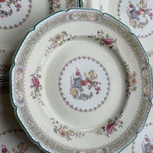 Puede incluir: Juego de seis platos de cena de cer&aacute;mica blanca con un dise&ntilde;o floral verde, dorado y blanco. Los platos tienen un borde festoneado y un centro elevado.