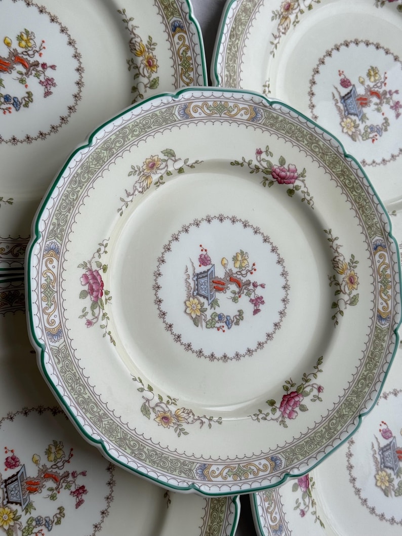 Puede incluir: Juego de seis platos de cena de cer&aacute;mica blanca con un dise&ntilde;o floral verde, dorado y blanco. Los platos tienen un borde festoneado y un centro elevado.