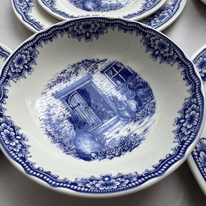 K&ouml;nnte beinhalten: Ein Set aus vier wei&szlig;en Keramiktellern mit blauen Blumendesigns und einer Szene mit Kaninchen in der N&auml;he eines Hauses. Die Teller haben einen gewellten Rand.