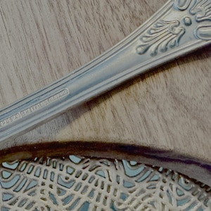 May include: Close-up of a silver spoon with an ornate design and the inscription "EPNS A1 SHEFFIELD ENGLAND".