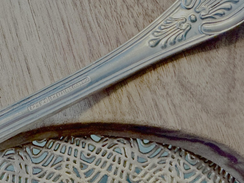May include: Close-up of a silver spoon with an ornate design and the inscription "EPNS A1 SHEFFIELD ENGLAND".
