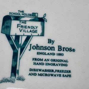 May include: A green and white ceramic plate with a mailbox design. The mailbox has a sign that reads "The Friendly Village". The plate is marked "By Johnson Bros. England 1883" and "From an original hand engraving". It also states "Dishwasher, freezer and microwave safe."