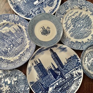 May include: A collection of blue and white ceramic dinnerware featuring various transferware patterns. The set includes plates and bowls decorated with detailed illustrations of historic buildings, landscapes, and floral borders in shades of blue.